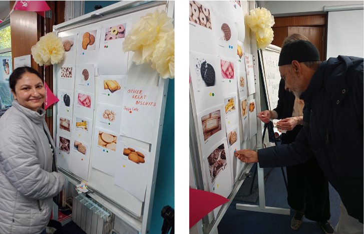 Two photos. One shows a woman standing next to a board and smiling. The setting looks to be a community centre. The board has pictures of different kinds of biscuits on it, onto which people have stuck small circular stickers in different colours. There is another pinned piece of paper that reads 'Other great biscuits. Jaffa cake'. The second photo shows the same board, and a man placing one of the stickers onto it.