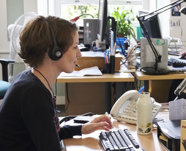 A staff member at the Down to Earth support service for people facing funeral poverty, sitting at their desk, wearing a headset with a computer in front of them.