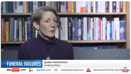 A screenshot of a Sky News report, showing a woman speaking in front of a wall of bookshelves. The text on the screen reads 'Funeral Failrure. Quaker Social Action. Lindesay Mace'.