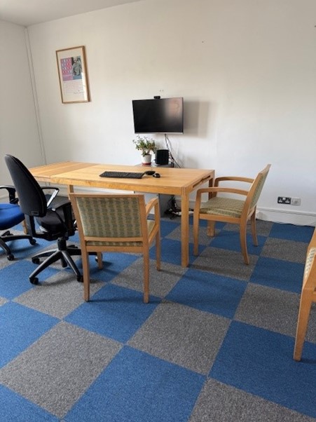 An office space with blue and grey carpet, a large desk and a wall-mounted monitor.